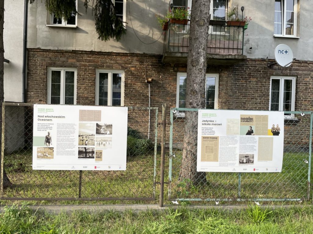 widok na dwie plansze wiszące na ogrodzeniu jako część wystawy Dawne Miasto Ogród Włochy na fotografii